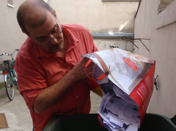 El traductor echando a la basura (reciclada, de papel), los manuscritos trabajados de la traducción de Abel.